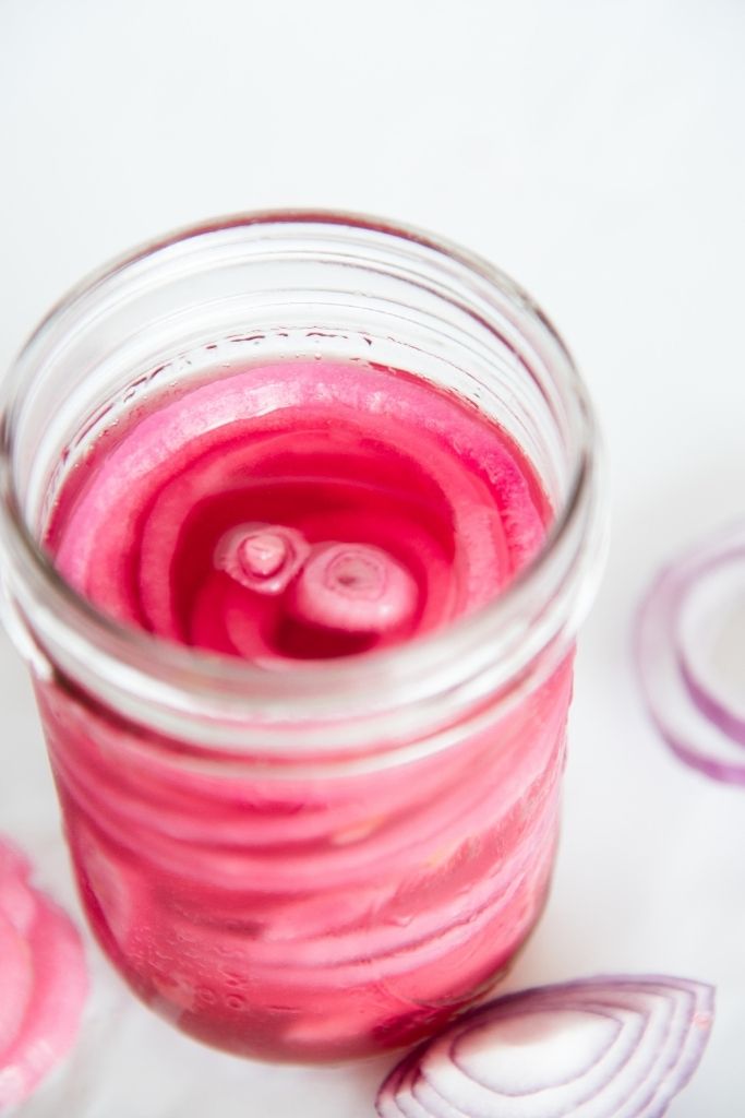 a jar pf pickled onions with onions slices around it