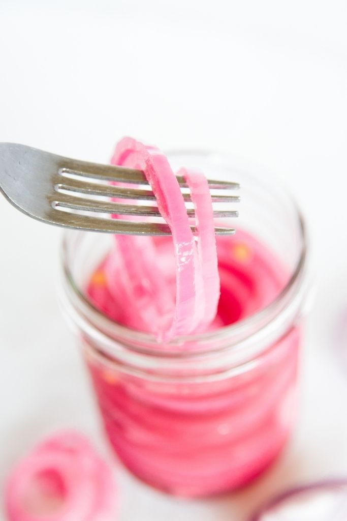 a close up of a forkful of pickled onions being held over a jar of onions