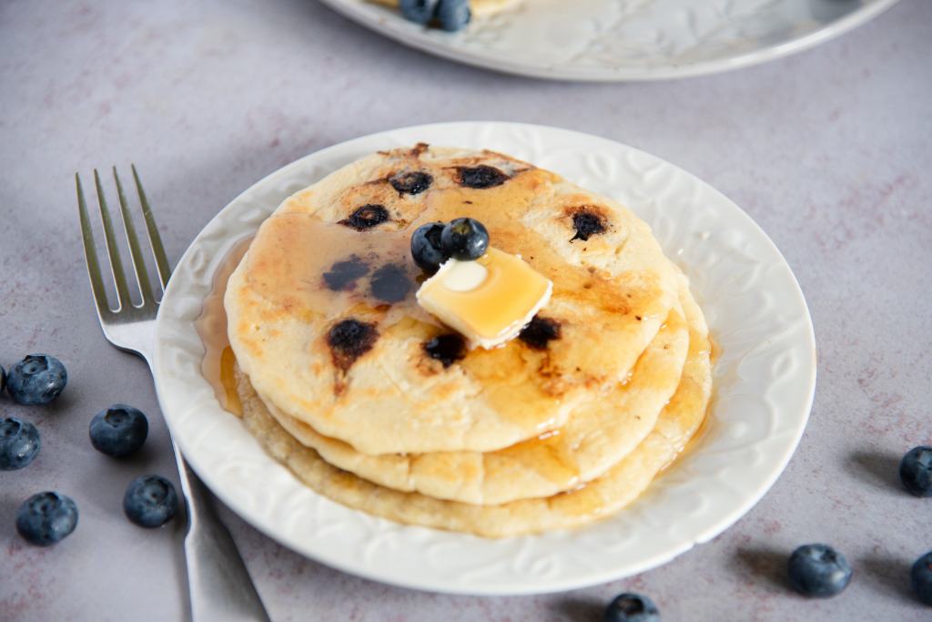a plate of blueberry pancakes with butter and syrup on top, there is also a fork next to the plate