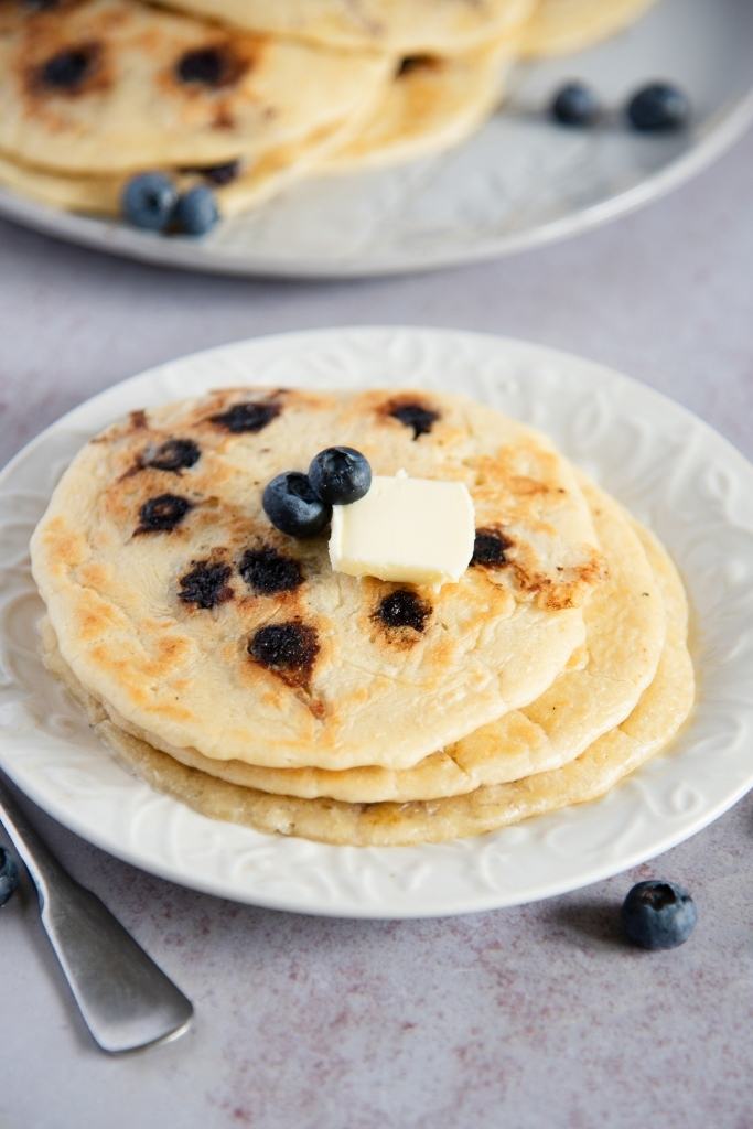 a stack of blueberry pancakes with a pat of butter and some blueberries on top of it
