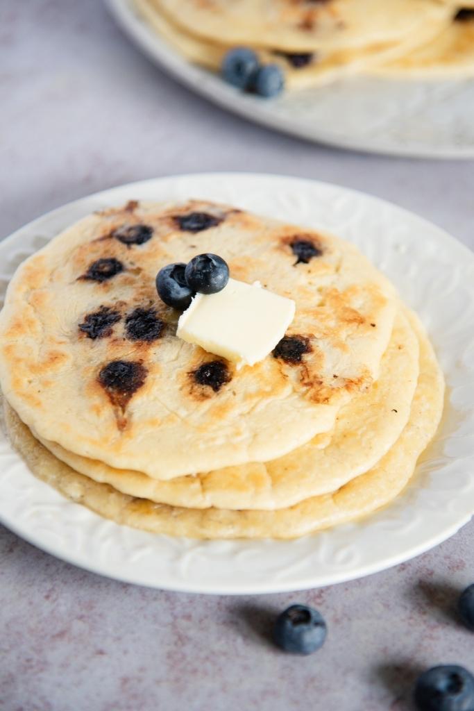 a close-up of a stack of blueberry pancakes with butter on top. 