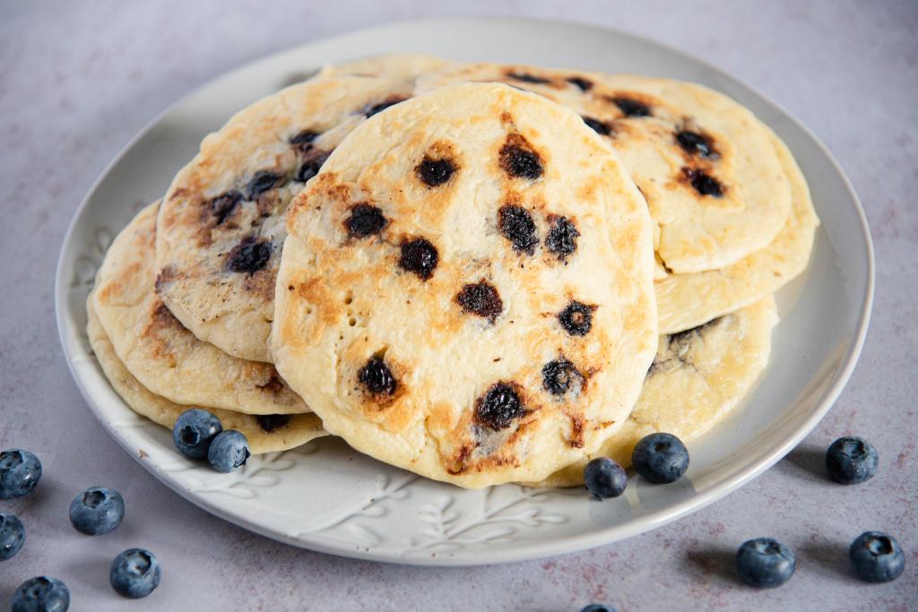a plate of blueberry pancakes, there blueberries scattered around the plate too.