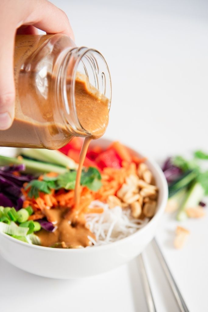 peanut dressing being poured over a bowl of spring roll salad