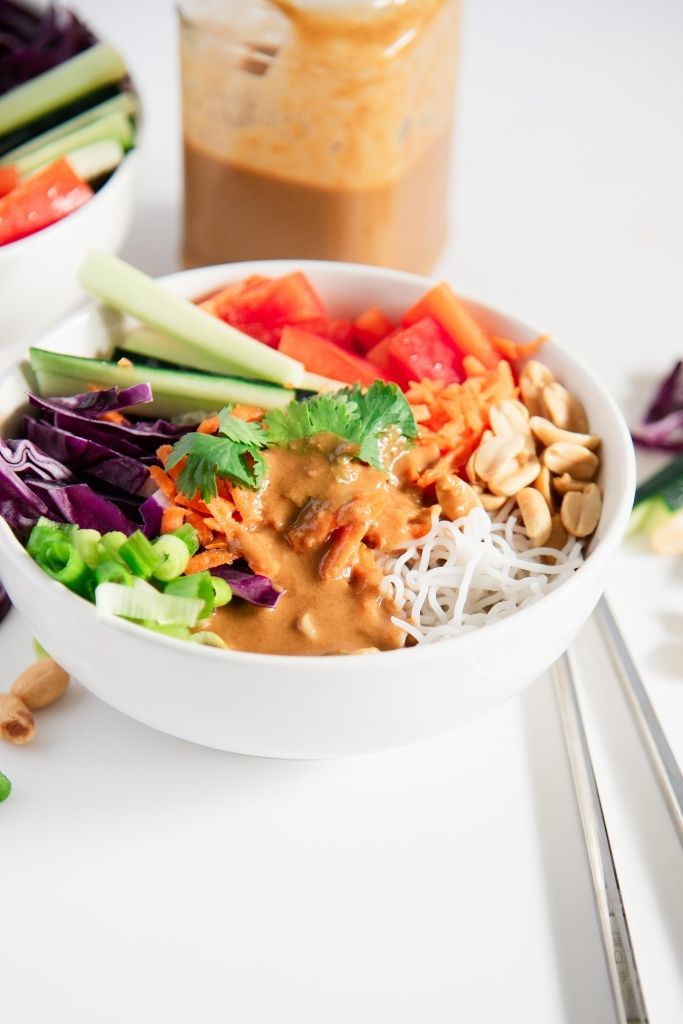 a bowl pf spring roll salad with peanut dressing on top. You can see the jar of dressing behind the bowl