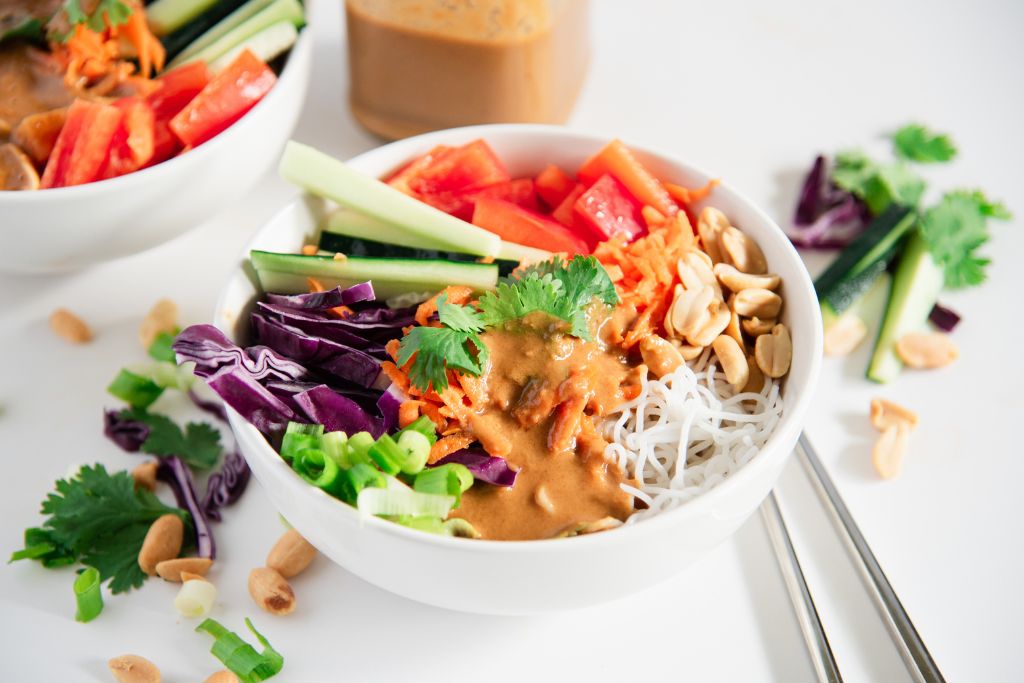 a bowl of spring roll salad with dressing on top. You can see part of another bowl, a jar of dressing and some chopsticks next to the salad as well