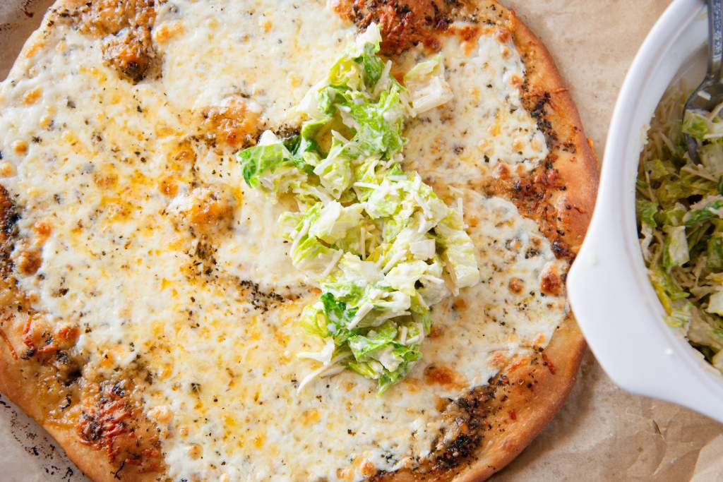 a baked cheese pizza with a spoonful of Caesar salad on it 