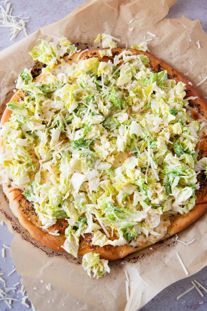 a baked pizza with Caesar salad speared over it 