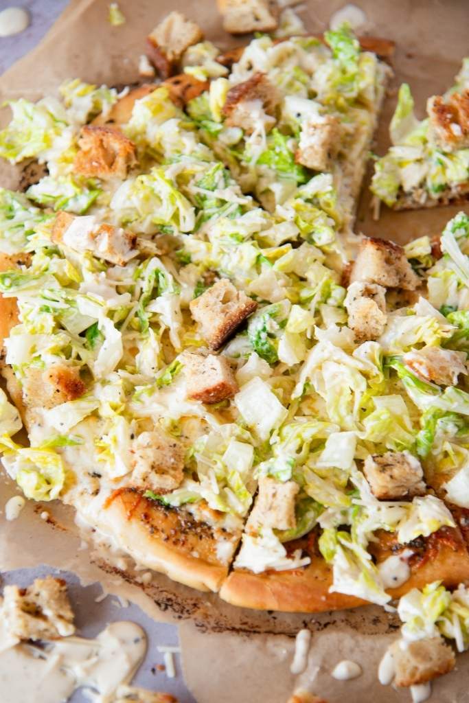 a close up of a sliced Caesar salad pizza