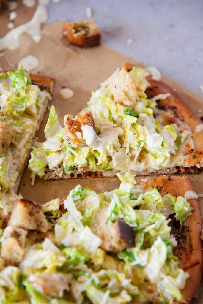 a close up of a slice of Caesar salad pizza 