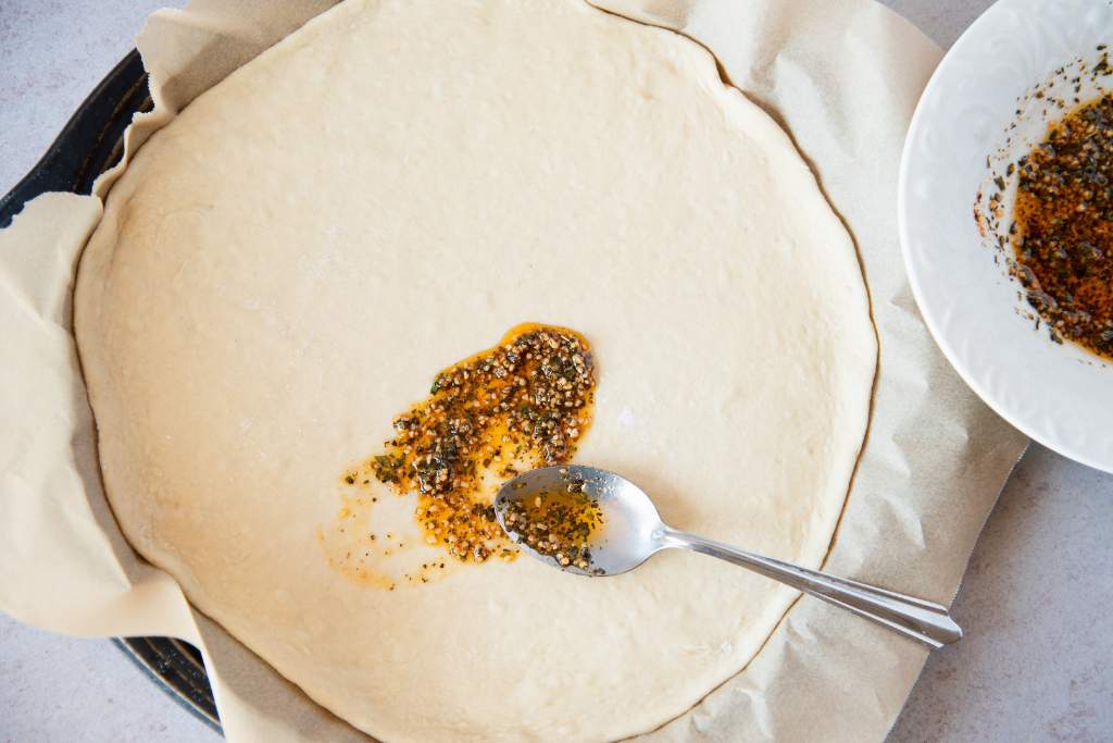 an uncooked pizza crust with oil and a spoon on it 