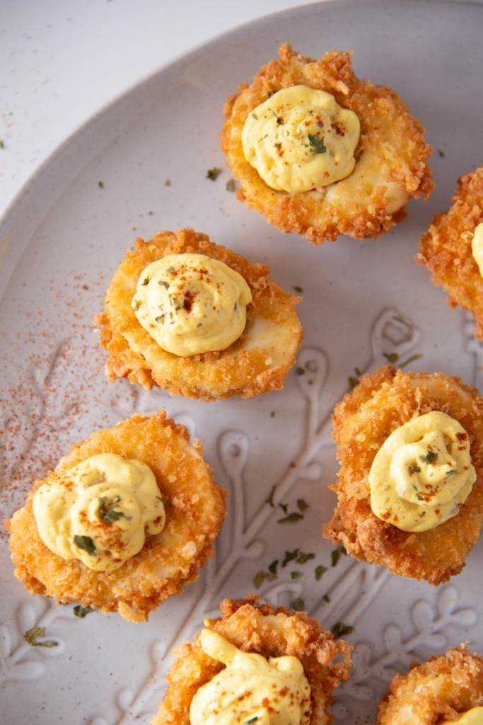 a cut off photo of a plate of deep fried deviled eggs with seasoning sprinkled around them