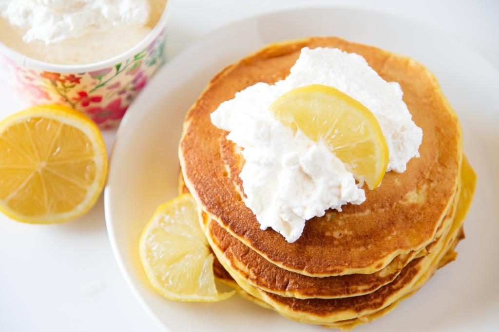 a stack of pancakes on a plate, the pancakes have whipped cream and a lemon slice on them 
