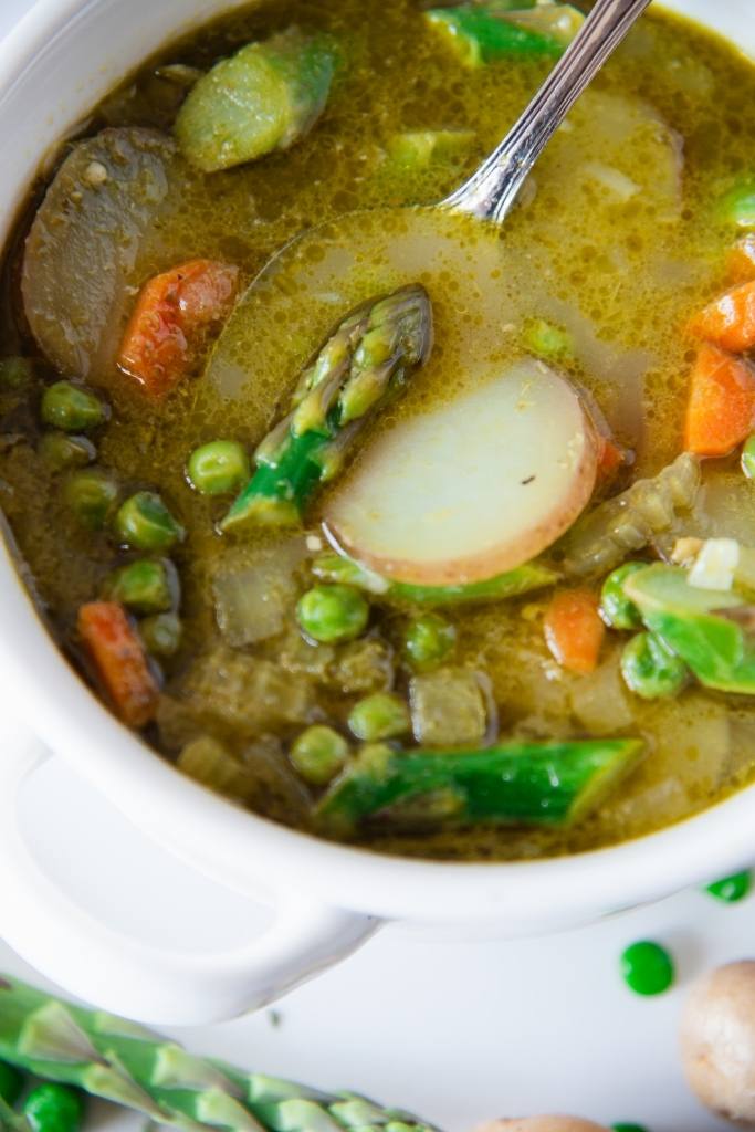 a close up of a spoon in a bowl of soup, there a potato slice and piece of asparagus on the spoon 