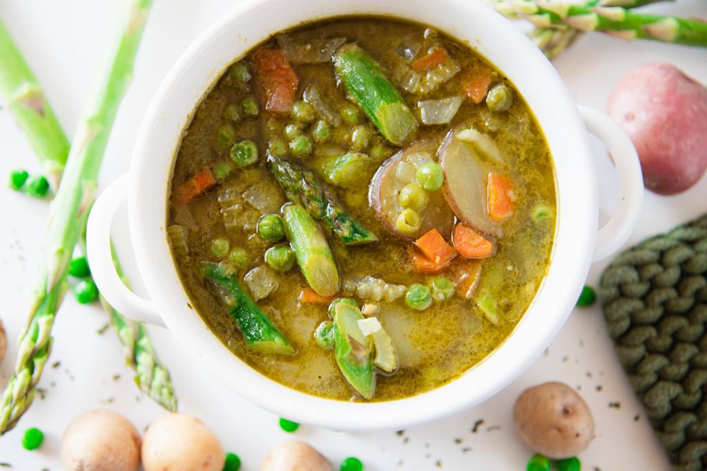 a bowl of springtime soup with fresh veggies scattered around it 