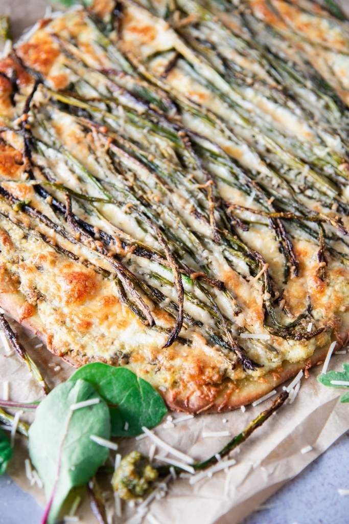 a close-up on an uncut pizza with some greens and shredded cheese by it 
