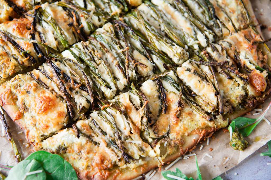a cut pizza with asparagus on it, there are some greens and some pesto around the pizza 