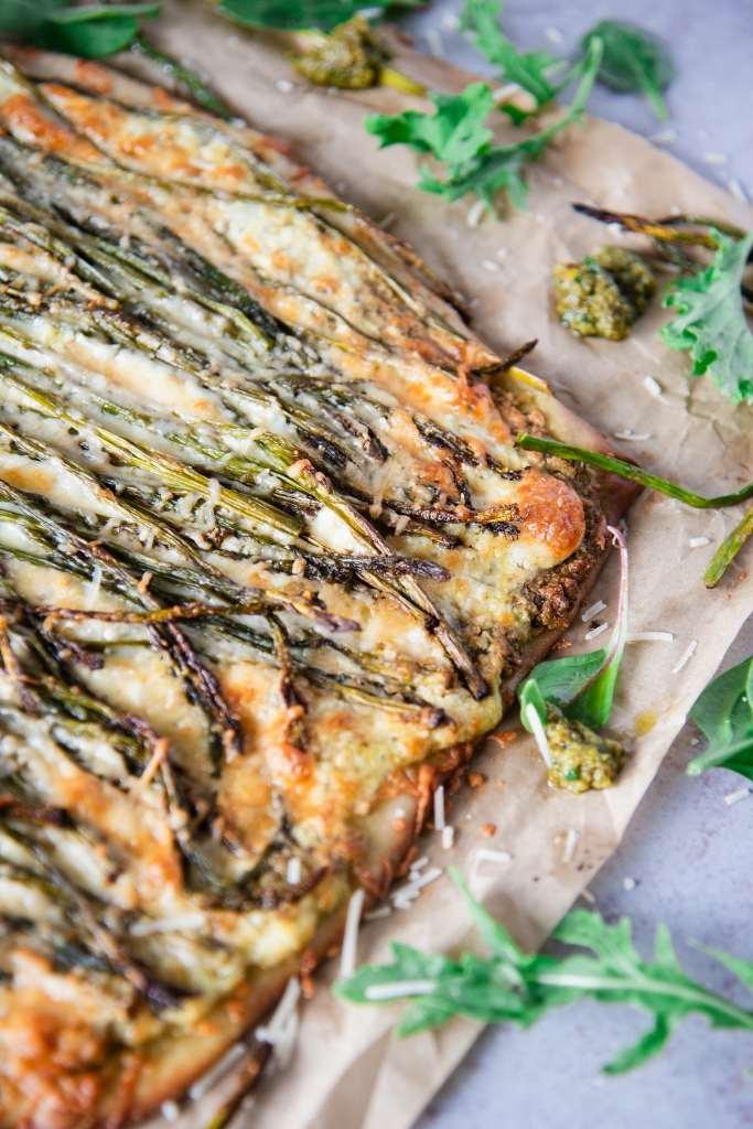 a close up on an uncut pizza with asparagus on it  