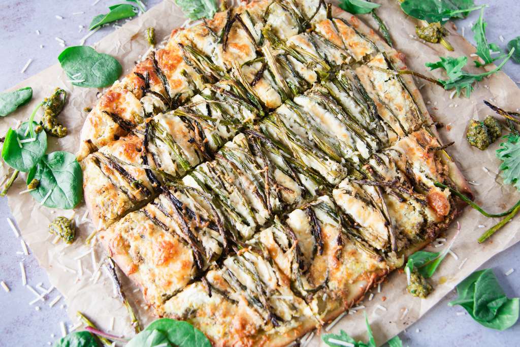 a cut pizza on parchment paper, there are some greens and pesto around it 