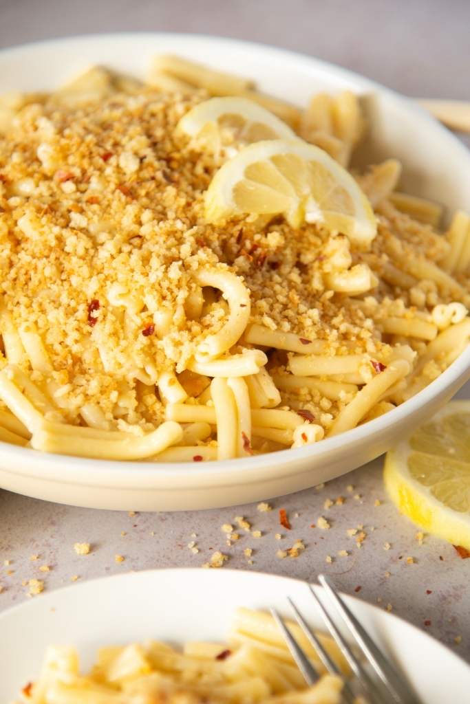 a close-up of a dish of pasta with breadcrumbs and lemon slices on top