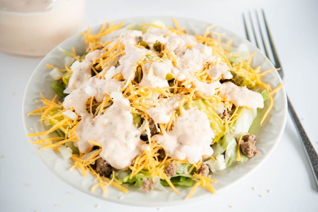 a bowl of salad with a fork next to it, and a jar of dressing behind it