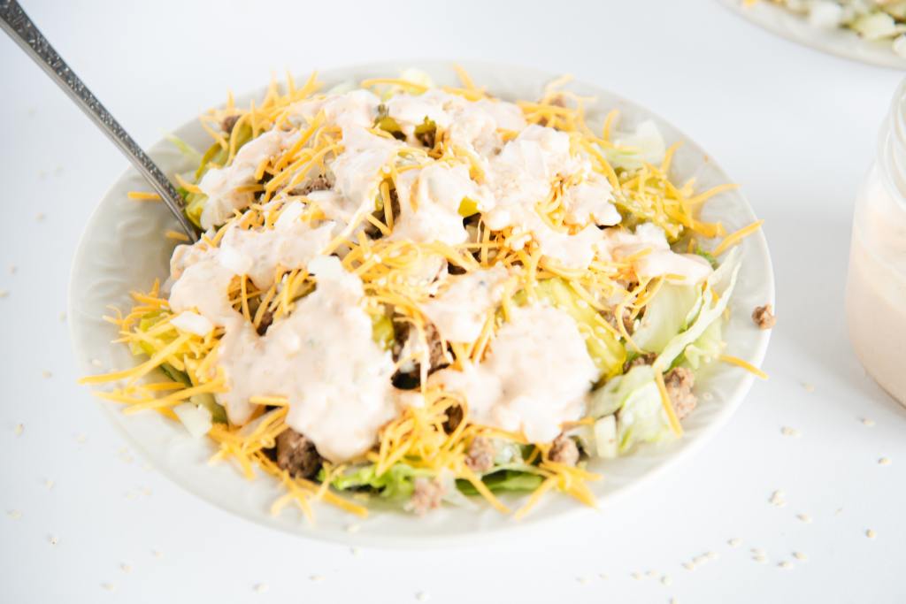 a bowl of salad with a fork stuck in it, you can also see part of a jar of dressing next to the bowl