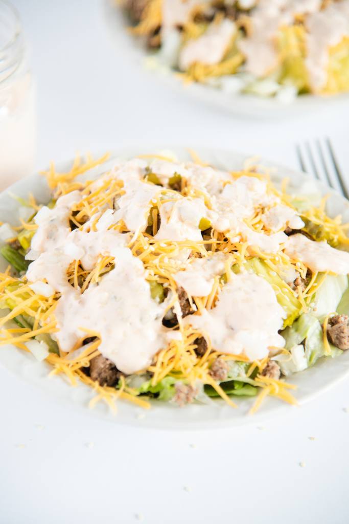a bowl of salad, you can see part of a fork and another bowl behind it
