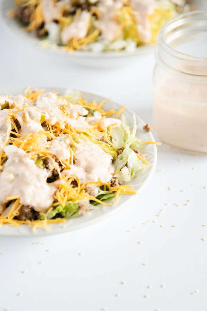a bowl of salad with a jar of dressing next to it. You can also see another bowl of salad behind it