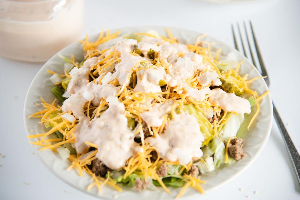 a bowl of salad with a fork and jar of dressing next to it