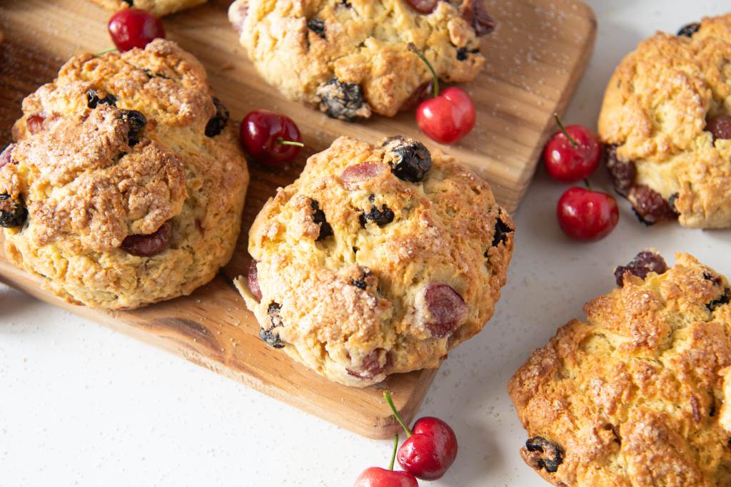 cherry scones set on a wooden tray with fresh cherries set around them 