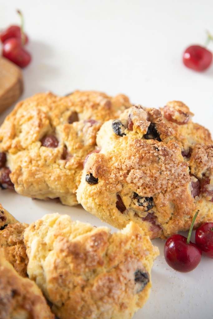 a close up of cherry scones with fresh cherries set around them 