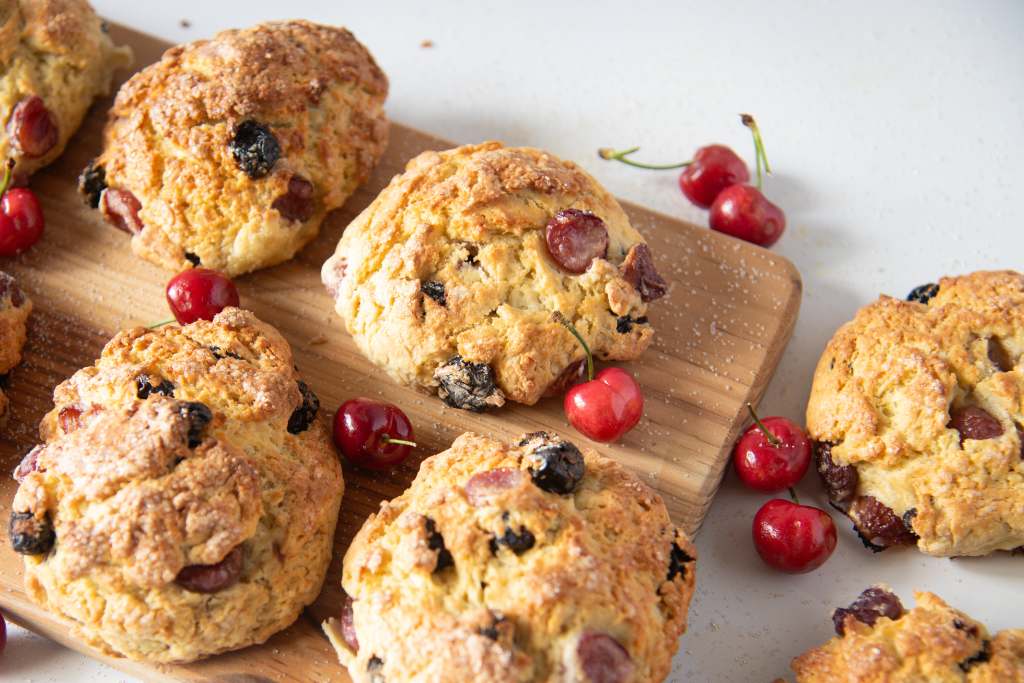 cherry scones on a wooden tray with sugar and fresh cherries around them 