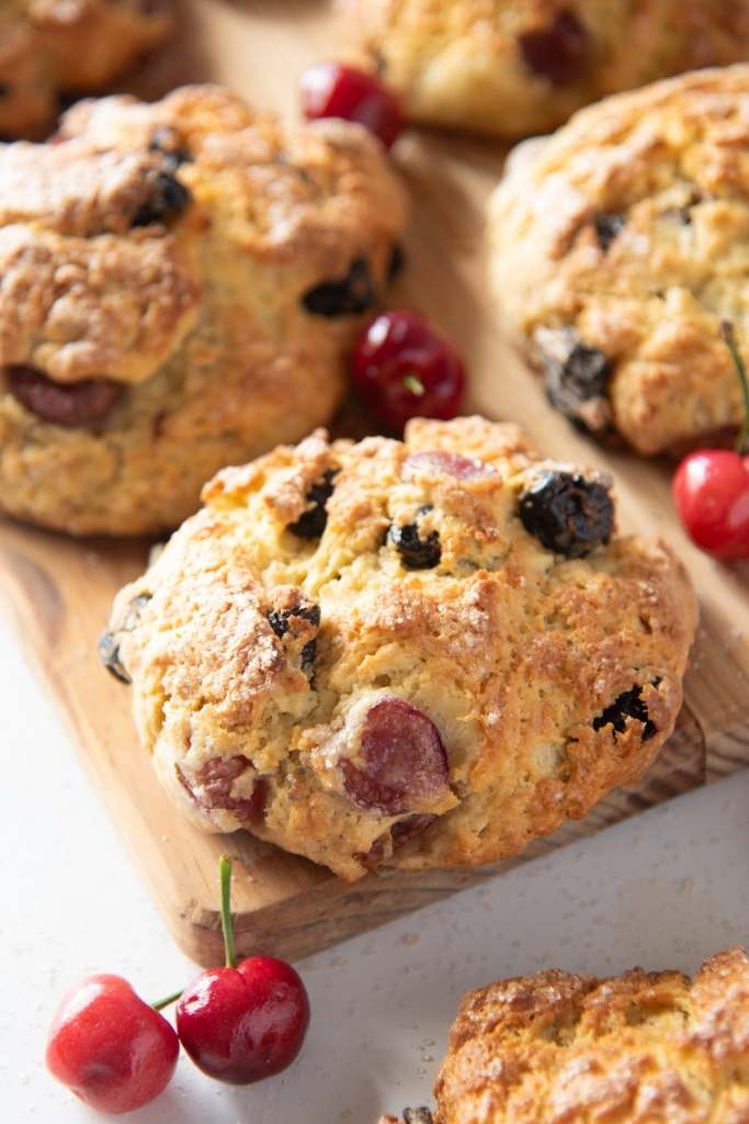a close up of a cherry scone on a wooden cutting board 