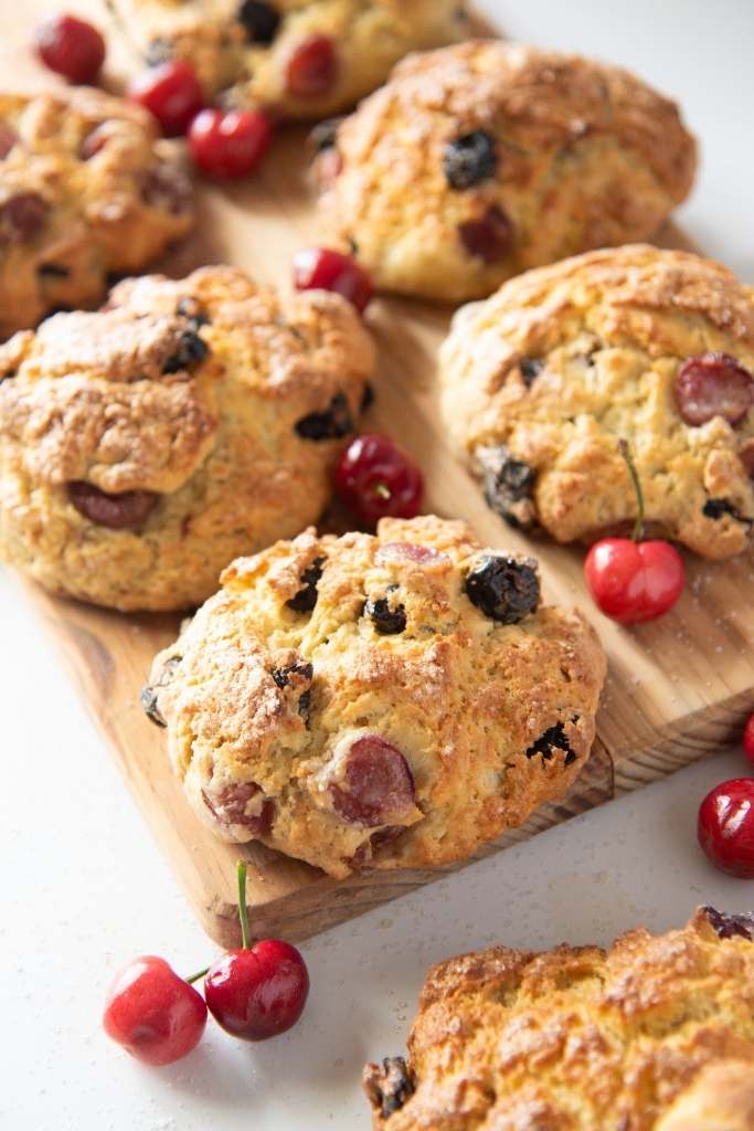 scones set out on a wooden tray wit cherries around them