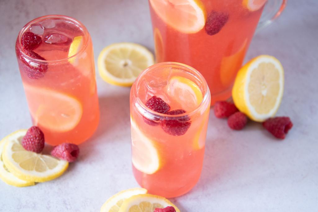 two glasses of lemonade with lemon slices and raspberries around them