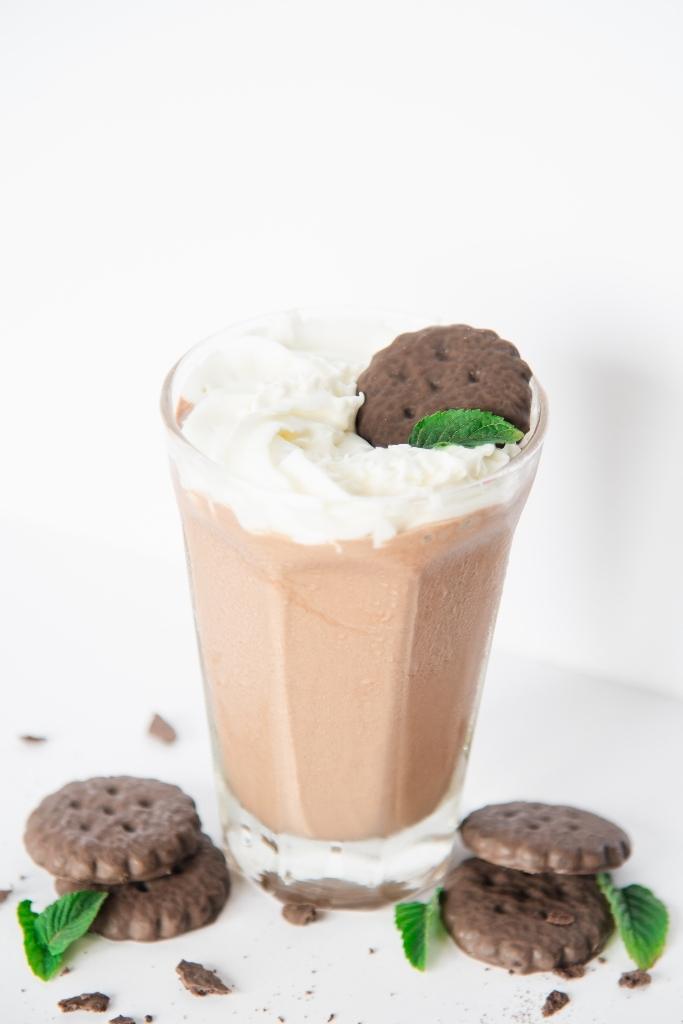 a shake topped with whipped cream, a cookie and a mint leaf