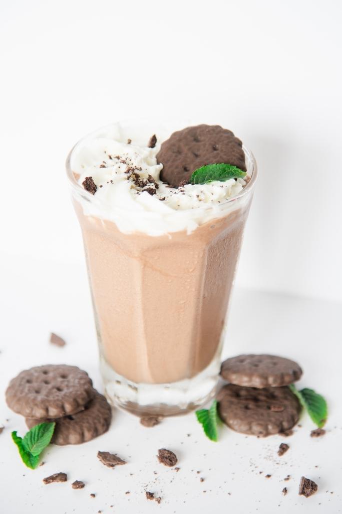 a shake with cookies and mint leaves around it, there is also whipped cream and a cookie on the shake