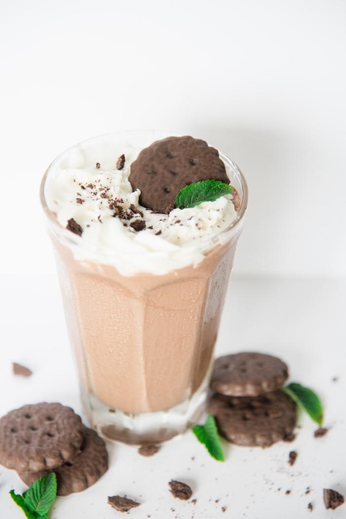 a milkshake with whipped cream, a cookie and a mint leave on top on it 