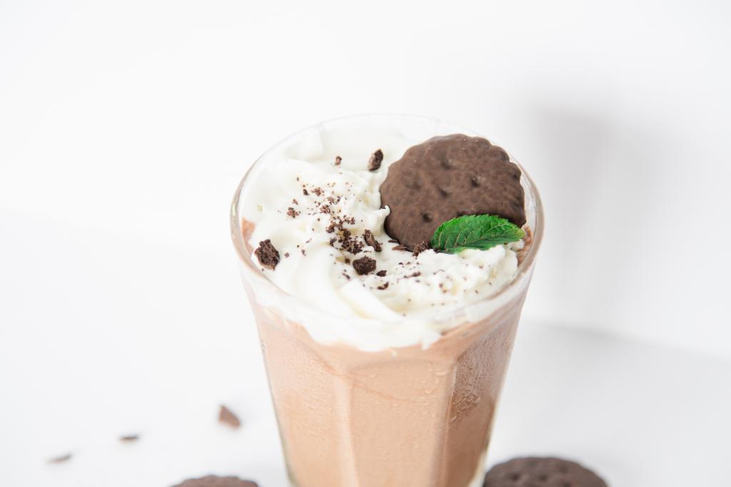 a close up of a milkshake that's been topped with whipped cream, a cookie, and a mint leaf