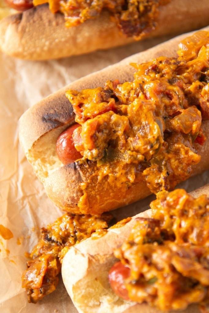 a close up of a hot dog with bacon onion topping on it