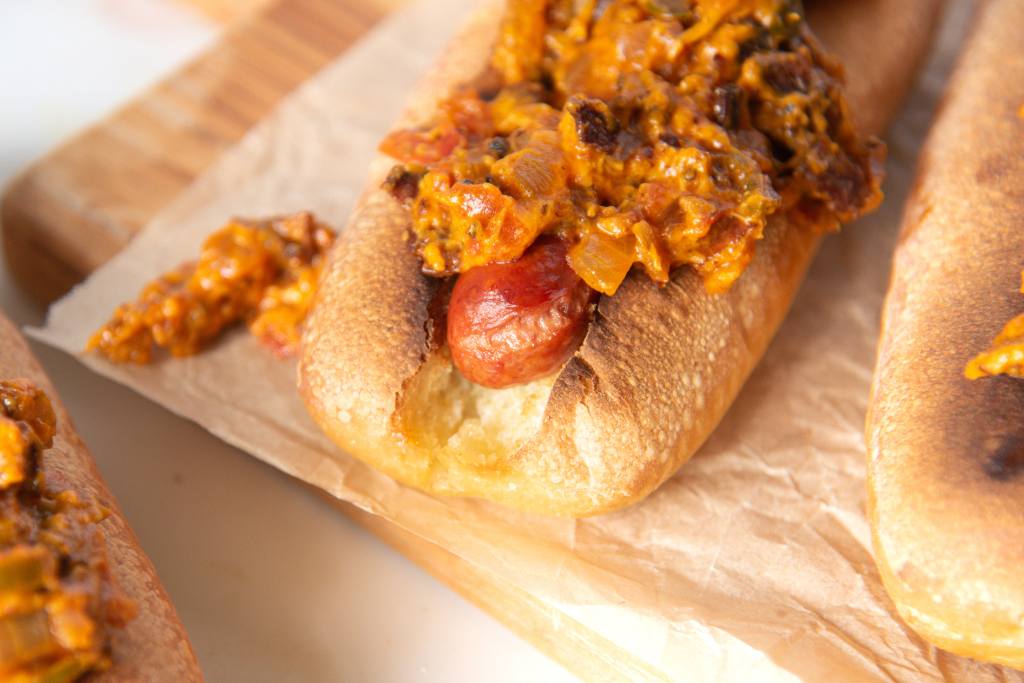 a close up of a hot dog with bacon onion topping on it