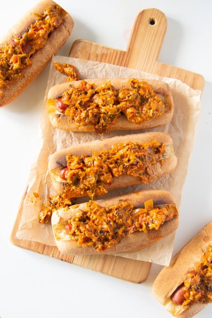 an overhead sot of three hot dogs on a wooden serving tray, you can see two hot dogs next to the tray as well.
