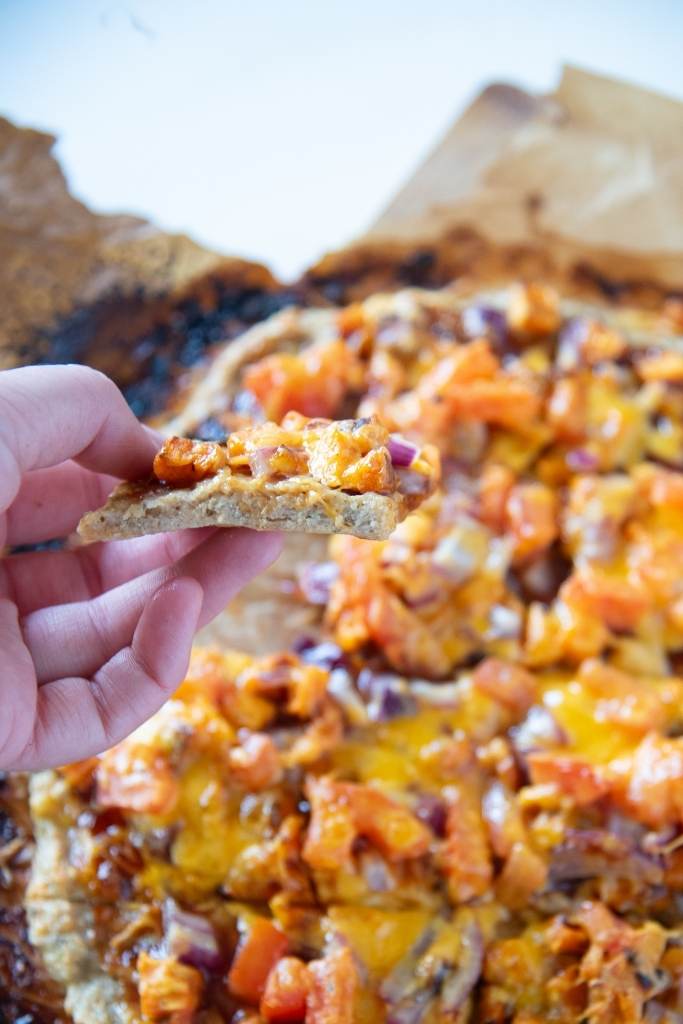 a piece of bbq chicken pizza being held over the rest of the pizza