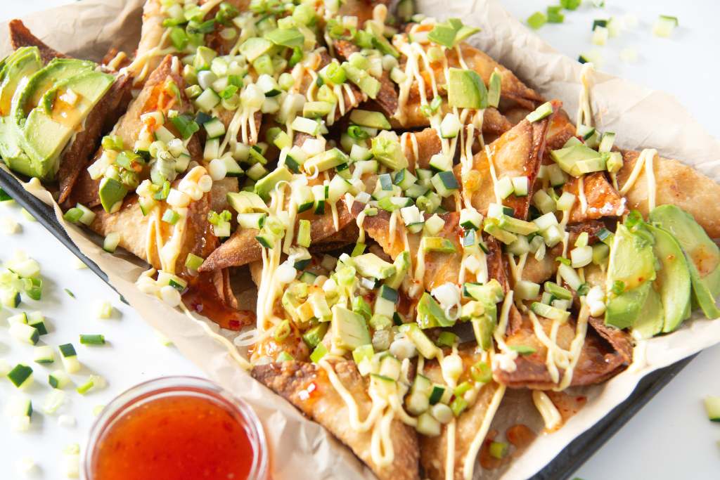 a tray og rangoon nachos with a dish of sweet chili sauce next to it, there are also some cucumber pieces and green onions around the tray