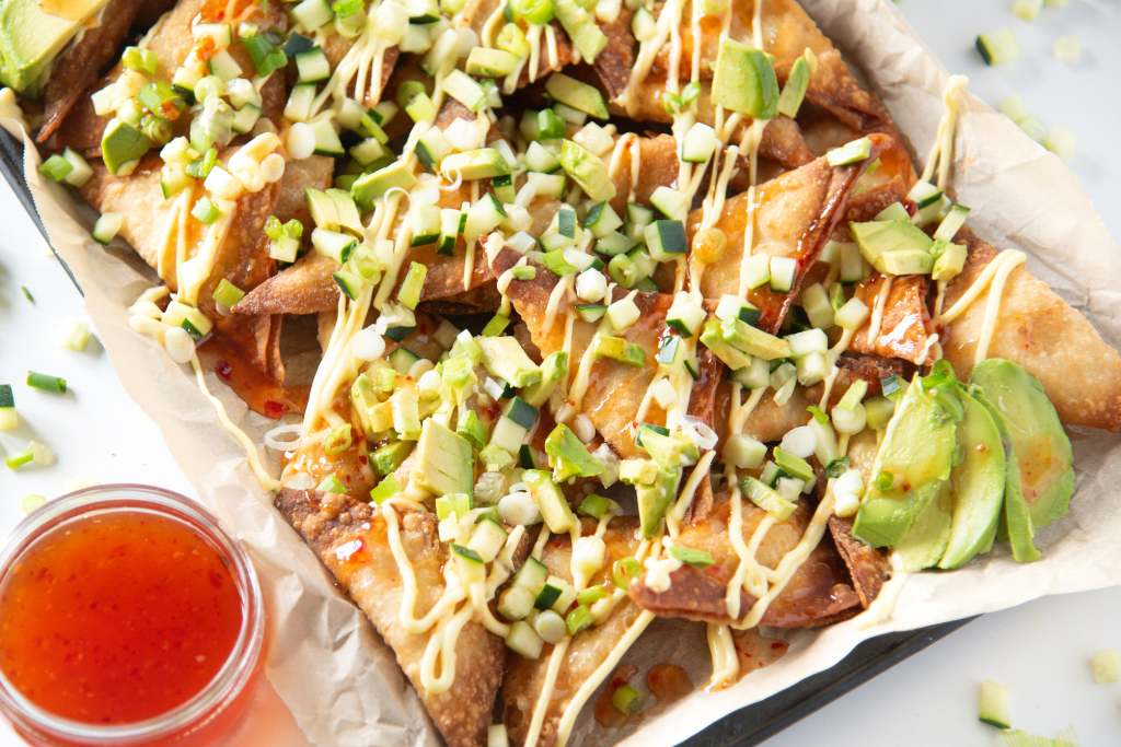 a tray of rangoon nachos with a dish of sweet chili sauce next to it 