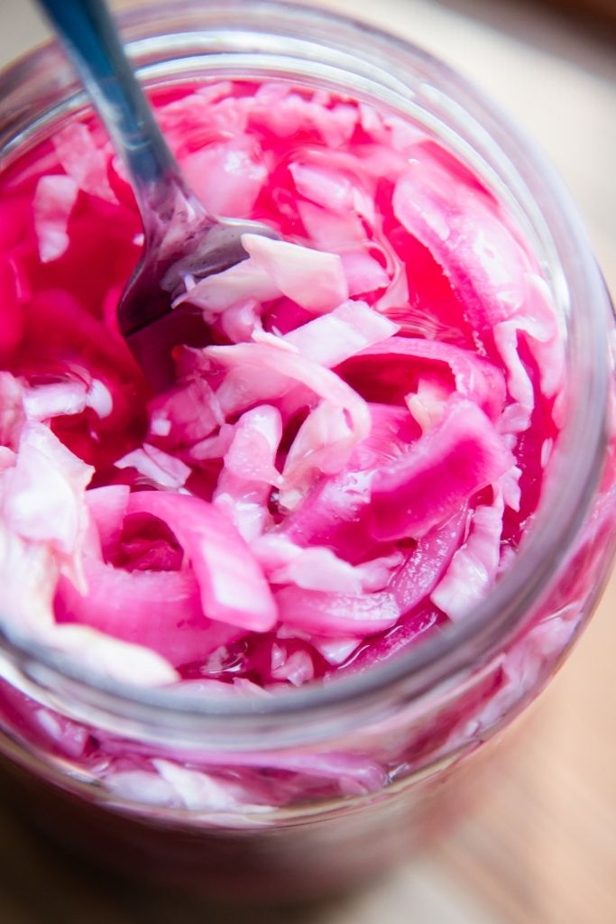 a close up of a fork stuck into a jar of pickled onions and cabbage 