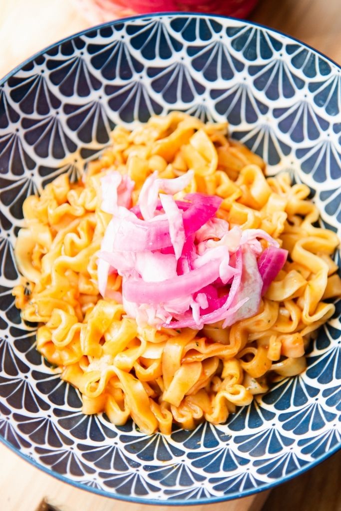 a bowl of noodles with pickled cabbage and onions on it 