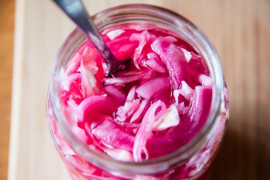 a jar of pickled cabbage and onions with a fork in it 