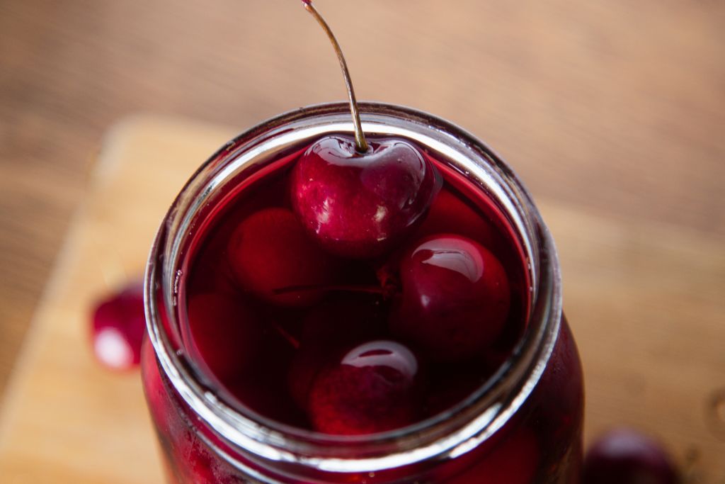 a close up of a cherry resting on the edge of a jar of cherries 
