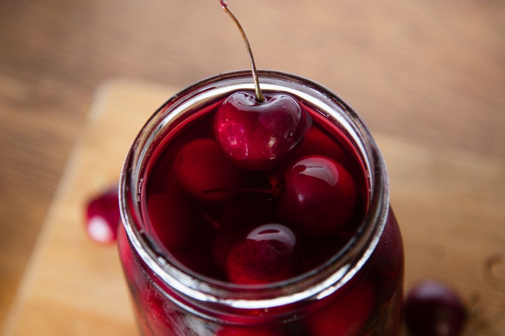 an open jar of pickled cherries, one cherry is resting on the edge of the jar 