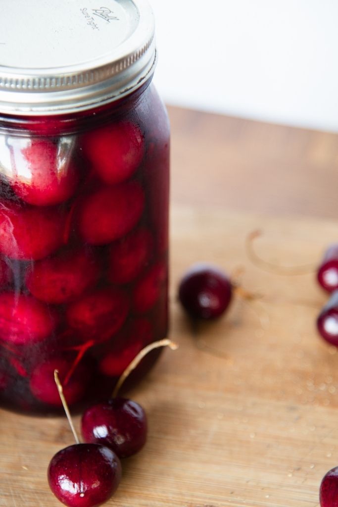 a jar of pickled cherries with fresh cherries next to it